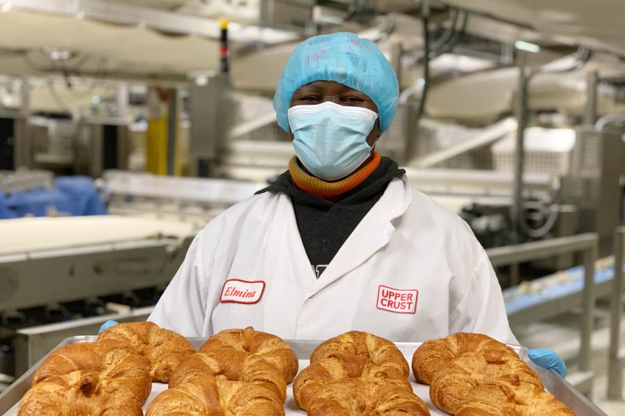 Upper Crust team member holding a tray of freshly baked pinched croissants