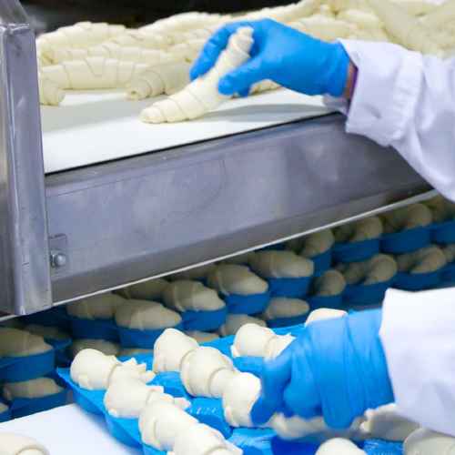 a Fiera Foods team member wearing food safety equipment carefully inspecting raw croissants