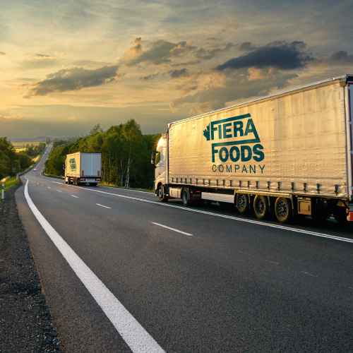two Fiera Foods trucks rolling down a highway at sunset