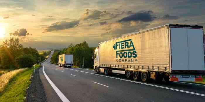 two Fiera Foods trucks rolling down a highway at sunset